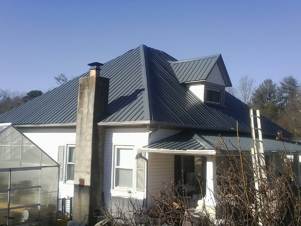 Dark blue standing seam metal roof on a white farmhouse with dormer — Slate & Tile Roof Repair by Roofing Brothers in Herington