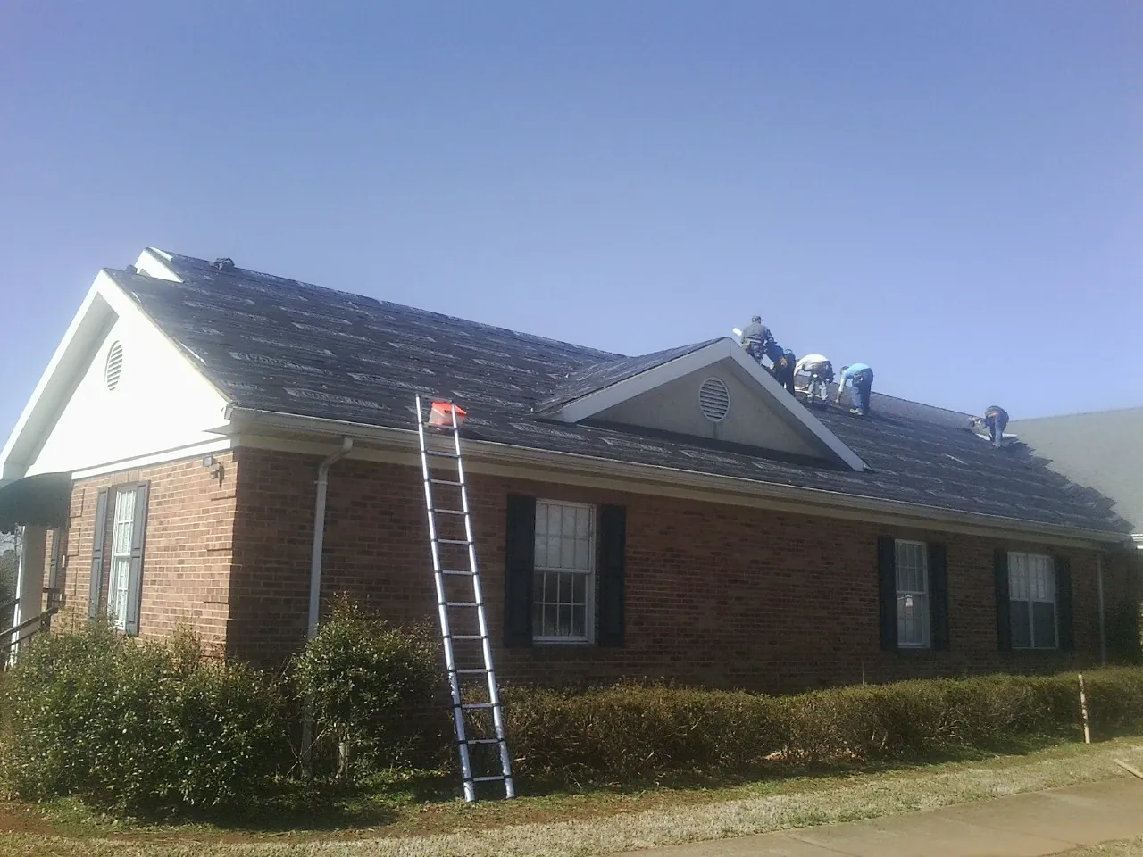 Crew tearing shingles off a brick ranch roof with a ladder set — Metal Roof Repair work by our crew in Herington