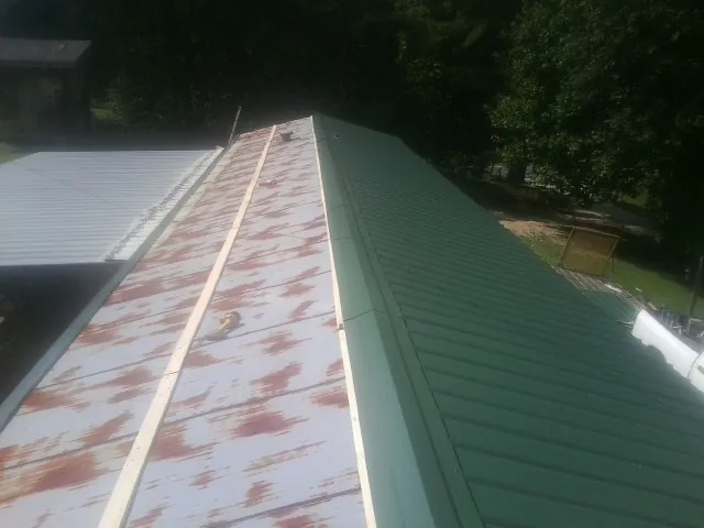 Old rusted panels beside newly installed green metal roofing — Wind Damage Roof Repair by Roofing Brothers in Herington