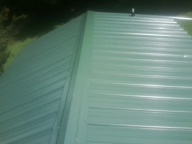 New green metal panels meeting at the ridge of a roof — Flat Roof Repair work by our crew in Herington
