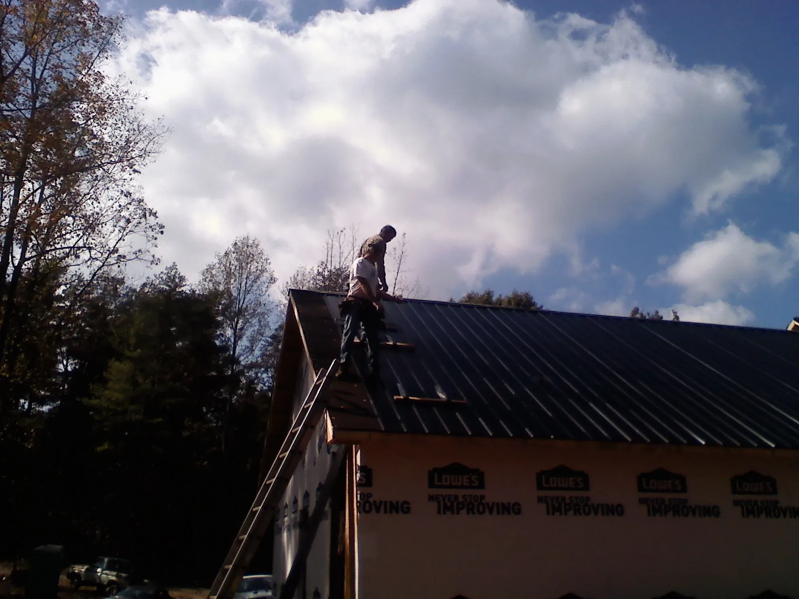 Roofer fastening dark metal panels high against a cloudy sky, from a Roof Inspection job in Herington