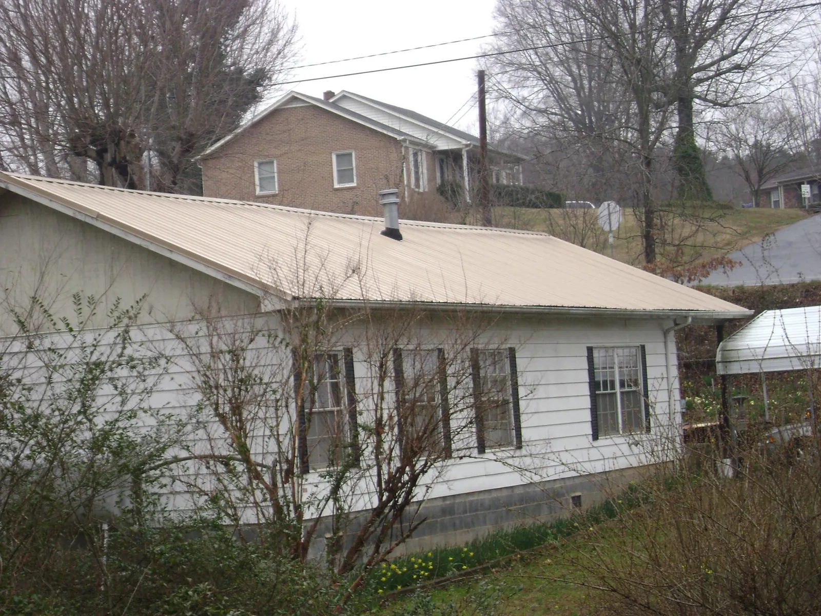 Tan metal roof on a white sided house set into a hillside — Commercial Roofing by Roofing Brothers in Herington