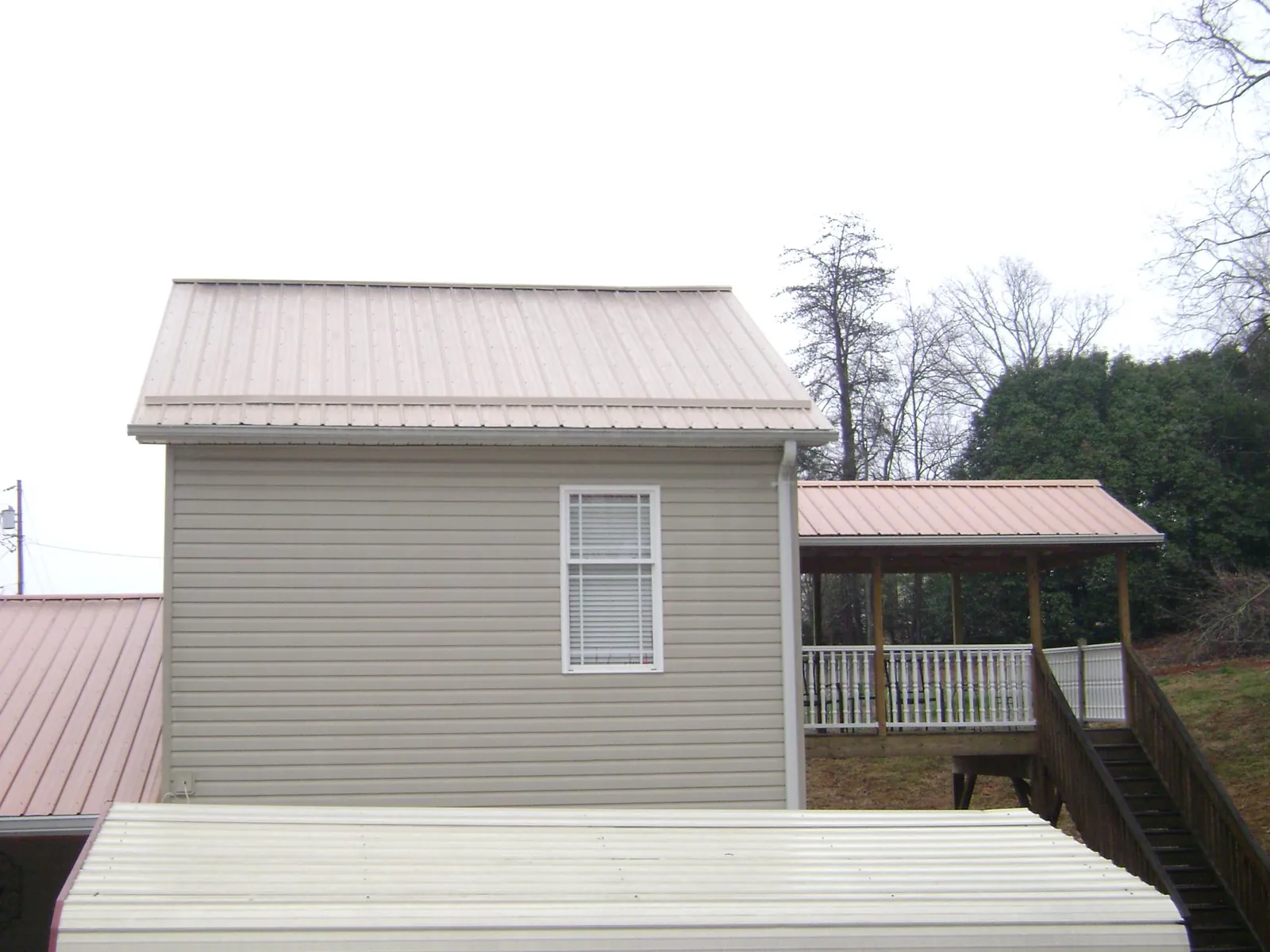 Tan metal roofs on a two story addition and attached porch, from a Roof Replacement job in Herington